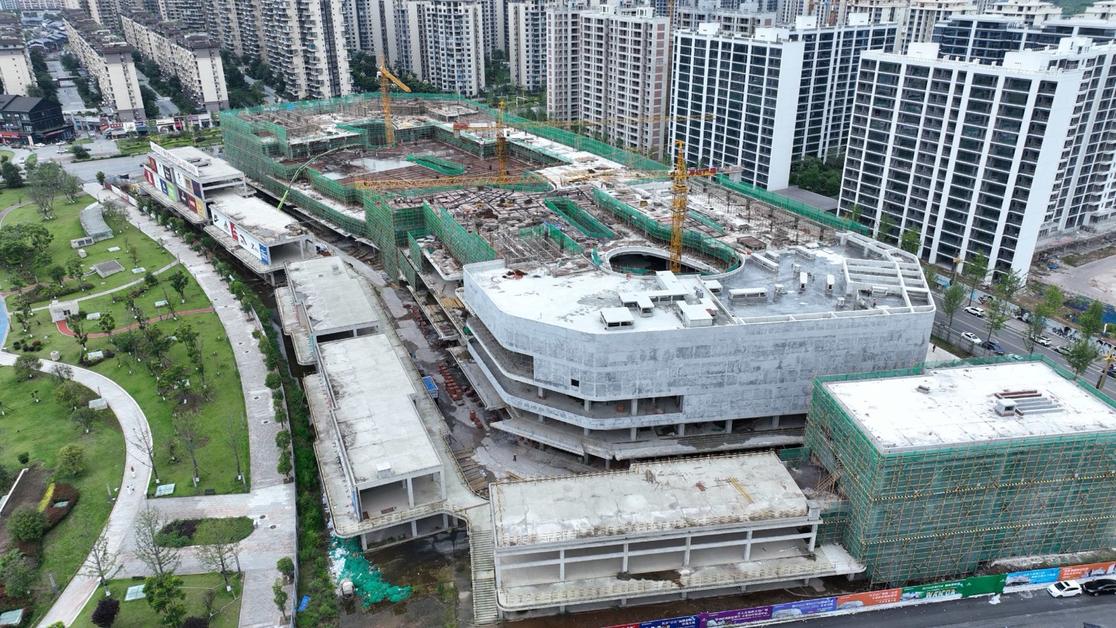 岳池万达广场工地近景，屋面施工面、脚手架、防护网和塔吊可见
